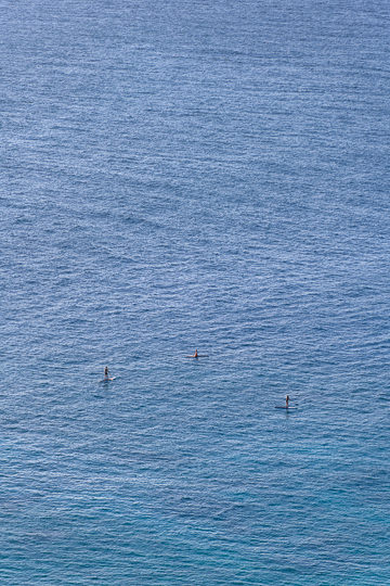 Three small paddleboarders in a big ocean.